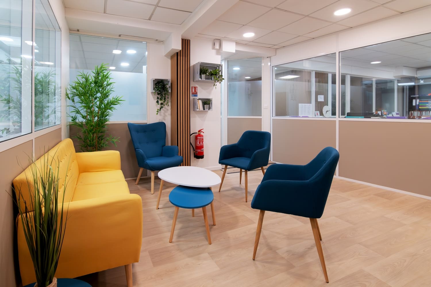 Coin salon lumineux avec canapé jaune et fauteuils bleus, parfait pour les pauses dans un espace de coworking